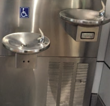 Two stainless steel water dispensers, with one being shorter in height and featuring a sign indicating it is designed for use by people with disabilities mounted above it